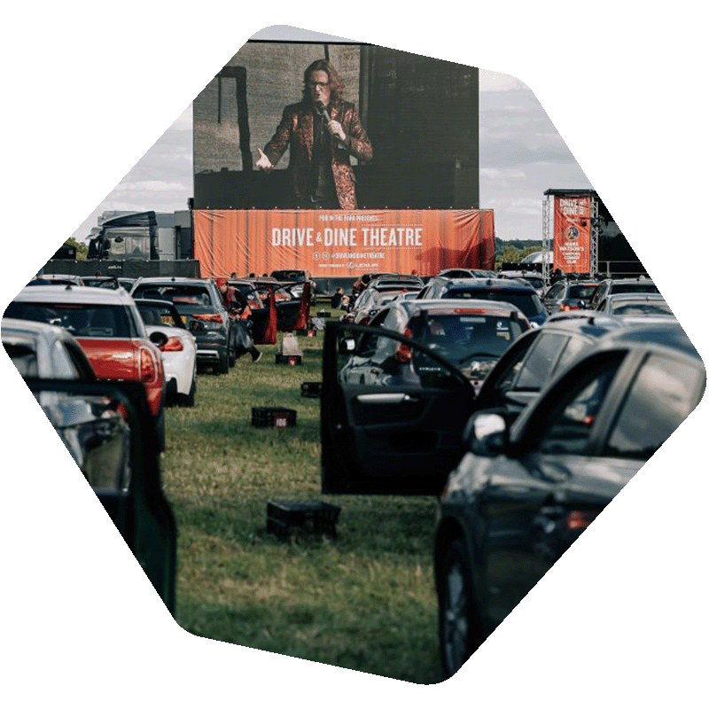Photo of cars parked in front of a large screen outside