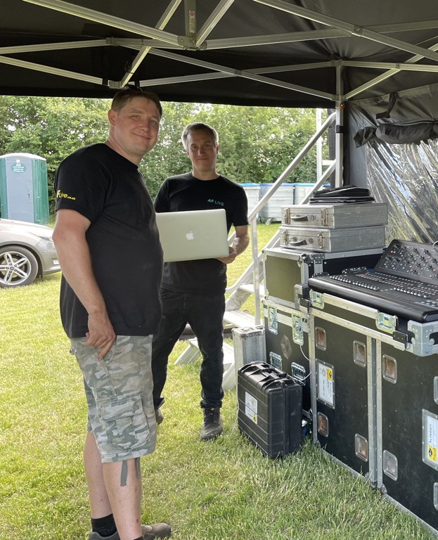 Two men smiling at the camera operating technical production